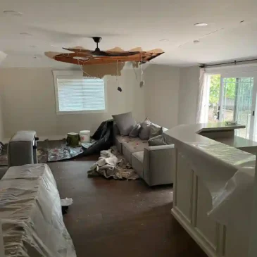 Living room ceiling collapsed after storm damage, showing debris and water intrusion before restoration.